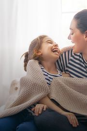 Mother and daughter sitting on bed laughing with each other